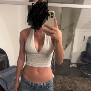 Glittrig vit halterneck croppad festtopp - Säljer en glittrig vit croppad halterneck topp med djup v-ringning. Toppens material har en skimrande finish och sitter tight över kroppen. Perfekt för dig som vill sticka ut med en snygg och trendig look. Nypris: 500