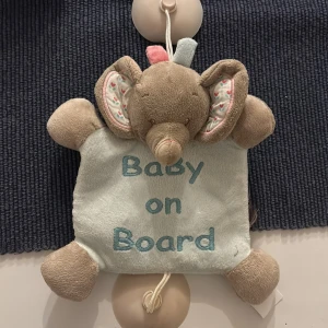 Baby on Board Elefant - Söt mjuk elefant med texten 'Baby on Board', perfekt för att fästa i bilen med sugproppar. Tillverkad i mjukt tyg, med fina detaljer på öronen. Ser ut att vara i mycket gott skick utan synligt slitage eller defekter.