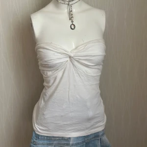 Vit bandeau tubtopp med twist - Säljer en vit bandeau tubtopp med snygg twistad detalj framtill. Toppen är axelbandslös och har en mjuk, stretchig känsla i bomullsmaterial. Perfekt för sommarens varma dagar och enkel att matcha med jeans eller kjol.