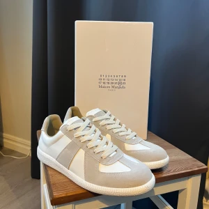 Maison Margiela vita och beige sneakers - Maison Margiela sneakers i vitt och beige med snygga paneler i mocka och skinn. Klassisk rund tå, platt sula och beige snörning. Säljer dom eftersom de finns inget bevis att skorna är äkta och är fortfarande ösäker, 🔥PRIS OCH ANNAT KAN ALLTID DISKUTERAS 🔥