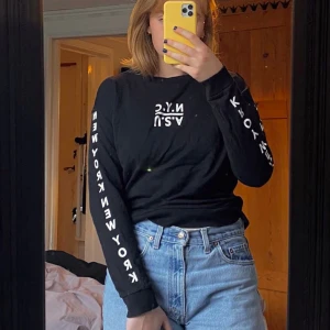 Svart långärmad tröja från H&M Divided - Svart långärmad tröja från H&M med vit text ”N.Y.C” och ”U.S.A” på bröstet, och ”NEW YORK” längs båda ärmarna.