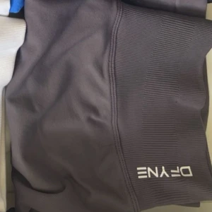 Grå tighta träningsshorts  - Säljer ett par grå, supertighta träningsshorts. De har låg midja och är gjorda i ett stretchigt syntetmaterial som sitter perfekt under gympasset. Shortsen har en diskret logga framtill och ribbade detaljer på sidorna för extra stil.