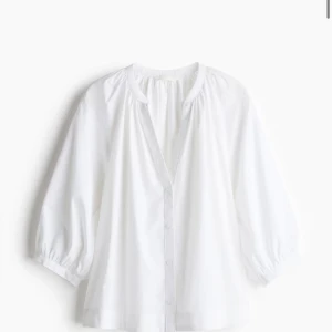 Vit v-ringad skjorta med puffärm - Luftig vit skjorta med v-ringning och knappar framtill. Skjortan har trekvartsärmar med puff och resår vid ärmslut, samt en avslappnad passform. Perfekt för en fräsch och stilren look.