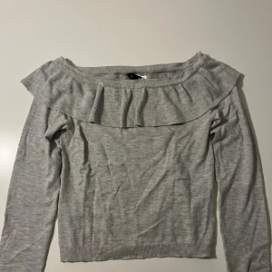 Grå offshoulder tröja med volang - Söt ljusgrå offshoulder tröja från hm i storlek XS. Tröjan har en bred volang längs halsringningen och är långärmad.