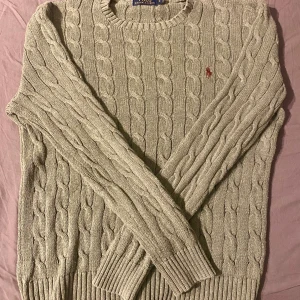 Grön kabelstickad tröja Polo Ralph Lauren - Kabelstickad grön tröja från Polo Ralph Lauren i bomull. Klassisk rund halsringning och långärmad modell med broderad logga på bröstet. Perfekt för lager-på-lager och snygg till jeans eller skjorta under.