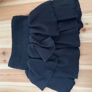 Svart volangkjol från Gina Tricot - Supersöt svart kortkjol från Gina Tricot med bred, smockad midja och flera lager volanger passar XS/S