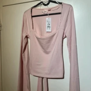 Ljusrosa omlottopp med knyt - Supersöt ljusrosa omlottopp från Bik Bok med långa, utsvängda ärmar och knyt i midjan. Toppen har en fyrkantig ringning med spetsdetalj och är gjord i mjuk bomull. Perfekt för dig som gillar romantisk och feminin stil.