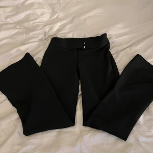 Svarta lågmidjade kostymbyxor från Gina Tricot  - Snygga svarta kostymbyxor med klassisk rak passform och en diskret bakficka. Byxorna har en stilren midja utan synliga detaljer framtill och är perfekta för en clean look. Materialet känns mjukt och följsamt, vilket gör dem bekväma hela dagen. Säljer då de är en aning kort för mig som är 165cm 