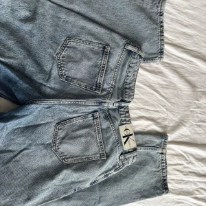 Calvin Klein ljusblå raka jeans - Säljer ett par klassiska ljusblå jeans från Calvin Klein Jeans med raka ben och normal passform. Jeansen har fem fickor, bälteshällor och metallknapp med CK-logga. Tillverkade i bomull för en skön känsla och snygg vintage-look.