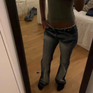 Levis bootcut jeans låg midja blå - Säljer ett par blå Levis jeans med bootcut och låg midja utan midjeband längst upp lik no waist jeans från Nelly. Jeansen har slitna detaljer och fransad kant upptill, klassisk femficksmodell och ljusare tvätt på låren och bak. Perfekta för en avslappnad och trendig look.