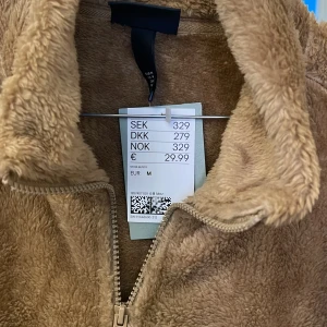 Beige teddyjacka med dragkedja M - Mysig beige teddyjacka från H&M i storlek M. Jackan har hög krage, hel dragkedja framtill och är tillverkad i mjukt teddy-material som ger en chill och trendig look. Perfekt för lager-på-lager och att hålla sig varm under kyliga dagar.