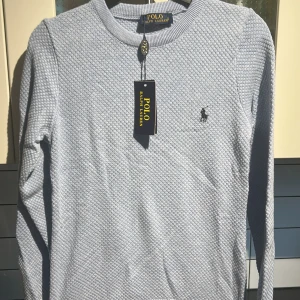 Ljusgrå bomullströja Polo Ralph Lauren - Snygg ljusgrå tröja från Polo Ralph Lauren i 100% bomull. Tröjan har ett diskret strukturmönster, rund halsringning och den klassiska broderade loggan på bröstet. Perfekt för dig som gillar stilrena och tidlösa plagg. Skriv inan köp