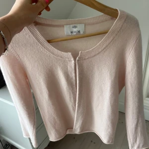 Ljusrosa kashmirkofta från Allude - Supermjuk ljusrosa kofta från Allude i kashmir. Enkel och stilren design med rund halsringning och långa ärmar. Perfekt för dig som gillar en clean look och vill ha något riktigt skönt och lyxigt i garderoben.