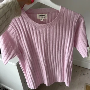Ribbad ljusrosa tröja Soft Goat - Superfin ljusrosa ribbad tröja från Soft Goat i storlek S. Tröjan har korta ärmar och rund halsringning, tillverkad i mjukt kashmirmaterial som känns lyxigt mot huden. Perfekt för dig som gillar stilrena och sköna plagg med lite extra färg.