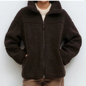 Mörkbrun teddyjacka med dragkedja - HELT SLUTSÅLD ‼️Mysig mörkbrun teddyjacka från Gina med hög krage och hel dragkedja framtill. Jackan har en loose passform och är tillverkad i fluffig syntet som ger en cool och chill look. Perfekt för kalla dagar när du vill vara både varm och stilren.