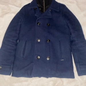 Kappa från Petrol Industries - Snygg mörkblå skepparkavaj från Petrol Industries med dubbelknäppning och klassisk krage. Jackan har två sidofickor, knappar vid ärmslut och quiltat foder på insidan. Perfekt för dig som gillar stilren och tidlös design.