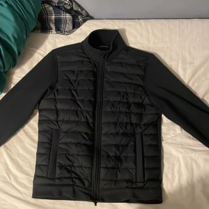 Svart quiltad dunväst från Dressmann - Svart dunväst från Dressmann i storlek M med quiltad framsida och slät baksida. Västen har hög krage, två sidofickor och hel dragkedja framtill. Perfekt för lager-på-lager och snygg till både jeans och hoodies.