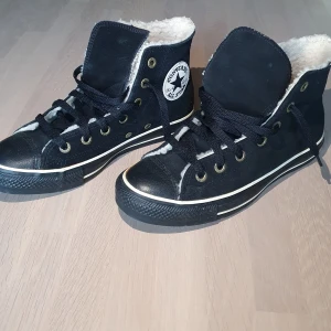  Oanvända Svarta Converse All Star high tops, 38:or. - Svarta oanvända Converse All Star high tops med vit pälsfoder på insidan, klassisk rund tå och platt sula. Skorna har snörning, metallöglor och den ikoniska All Star-loggan på sidan. Utsidan är i mocka och insidan är fodrad för extra värme. Perfekt för dig som vill ha en cool och varm sneaker.storlek 7,5 (38)dam, herr 5,5.