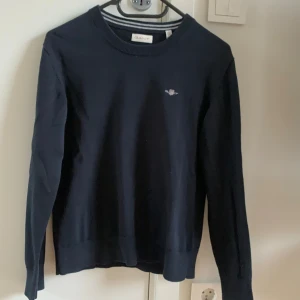 Mörkblå bomullströja från GANT - Snygg mörkblå tröja från GANT i mjuk bomull. Klassisk rund hals och långärmad modell med diskret broderad logga på bröstet. Perfekt för dig som gillar stilrena och enkla plagg. Passar dig som vill ha en normal passform.