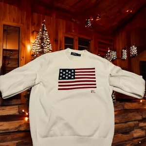 Vit stickad tröja Polo Ralph Lauren - Vit stickad tröja från Polo Ralph Lauren med amerikansk flagga broderad på bröstet och RL-detalj i rött. Rund hals, ribbade muddar och långärmad. Perfekt för dig som gillar klassisk stil med en twist.
