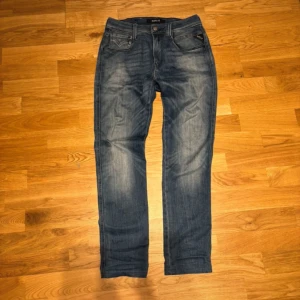 Replay blå jeans anbass - Snygga blå jeans från Replay anbass med klassisk femficksdesign och raka ben. Jeansen har coola slitningar och kontrastsömmar, samt Replay-logga på bakfickan. Passar dig som gillar en tidlös och avslappnad stil. De är dock  uppsydda så att dem är 30 i midja och 28 i längd men det står 30 32.