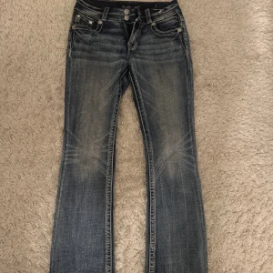 Miss Me blå bootcut jeans med broderi - Snygga blå jeans från Miss Me med bootcut passform och coolt broderi samt nitar på bakfickorna. Jeansen har låg midja, slitningar och kontrastsömmar. Dubbelknapp och dragkedja fram. Perfekt för dig som gillar detaljer och unik stil.