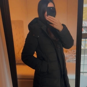 Svart lång pufferjacka med huva - Säljer en svart pufferjacka från Mango med lång passform och huva. Jackan har quiltad design, dragkedja framtill och praktiska sidofickor. Använd endast vid ett par tillfälle, helt i nyskick. Storlek XS, passar både  XS och S.