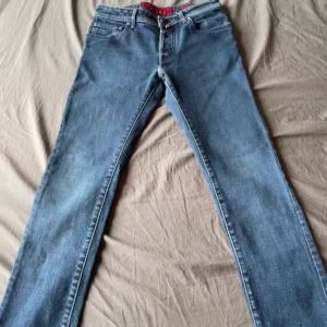 Blå jeans från Jacob Cohen - Snygga blå jeans från Jacob Cohen med klassisk femficksdesign och kontrastsömmar. Byxorna har en rak passform och detaljer som röd insida i midjan och patch med logga bak. Perfekta för dig som gillar stilrena och tidlösa jeans.kan prutas ner 