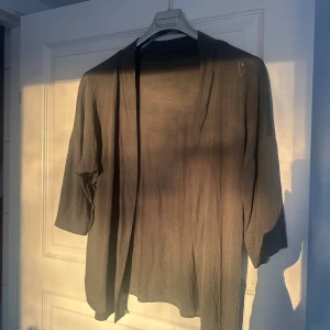 Grön kofta från Everyday Hero - Snygg och tunn grön kofta från Everyday Hero i storlek S. Koftan har öppen front, trekvartsärm och är gjord i mjuk viskos. Perfekt att slänga över en t-shirt för en chill look. Enkel design utan knappar eller dragkedja.