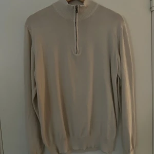 Beige half zip-tröja Oscar Jacobson - Snygg beige långärmad tröja från Oscar Jacobson med ribbad krage och half zip-dragkedja framtill. Tillverkad i 100% bomull för en mjuk och skön känsla. Perfekt för dig som gillar stilrena och enkla plagg med en clean look.  True to size med en aningen slimmad passform.  Den sanna färgen på tröjan är närmast som den ser ut på bild 3.  Kan skicka mått ifall det behövs.