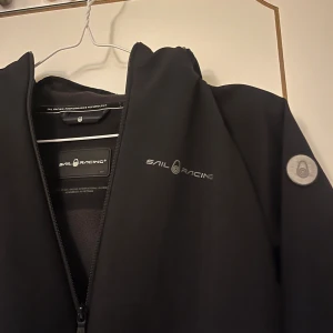 Svart vindjacka från Sail Racing - Svart vindjacka från Sail Racing med stilren design och logga på bröstet och ärmen. Inga fläckar eller liknade sista bilden va de bara spegel som va smutsig. Nypris 1100 