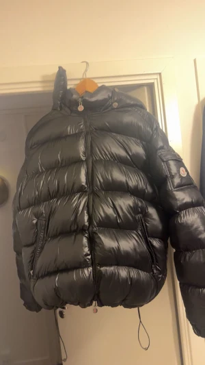 Svart Moncler Maya Jacka - Säljer en svart pufferjacka från Moncler med glansig finish och huva. Aldrig använt jackan och den är helt ny pris går diskuteras!