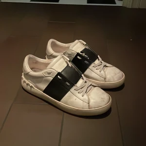 Valentino Open sneakers vit/svart - Säljer ett par Valentino Open sneakers i vitt skinn med bred svart läderpanel över snörningen. Snygga nitar längs hälen ger extra edge. Rund tå och platt sula, klassisk och stilren design som sticker ut. Hör av dig vid frågor eller funderingar ;) behövs rengöras litegrann, sedan ser dem prima ut! 🤩