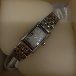 Mockberg silverfärgad rektangulär klocka - Stilren klocka från Mockberg med rektangulärt ur och romerska siffror. Klockan har en länkad armlänk i silverfärgat metall och levereras i originalask med extra länkdelar. Perfekt accessoar för dig som gillar klassisk och tidlös design. Nypris 1900kr