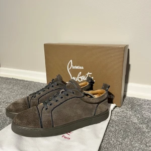 Gråa  mocka sneakers Christian Louboutin - Snygga Gråa sneakers från Christian Louboutin i mjuk mocka med svarta snören och klassisk röd sula. Rund tå och platt sula ger en clean look. Kommer med originalkartong, dustbag och tillbehör. Perfekt för dig som gillar exklusiva detaljer och stilren design.FRÅGA OM FLERA BILDER
