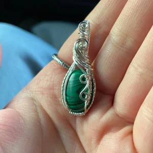 Silverberlock med konstgjord malakit  - Unikt halsband med en droppformad grön sten, infattad i intrikat virad silvertråd. Stenen har naturliga mönster i olika gröna nyanser och silvertråden är formad i snygga snirklar som ger ett bohemiskt och konstnärligt uttryck.