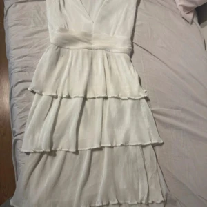 Vit studentklänning med volanger - Superfin vit långklänning med flera lager volanger och v-ringning. Klänningen är ärmlös och har en markerad midja. Nypris = 1000 kr