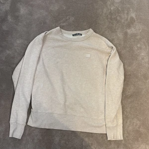 Beige sweatshirt från Acne Studios - Säljer en stilren beige sweatshirt från Acne Studios med klassisk rund hals och diskret logopatch på bröstet. Tröjan har långa ärmar och är gjord i mjuk bomull, perfekt för chill dagar. Enkel och clean design som funkar till allt.