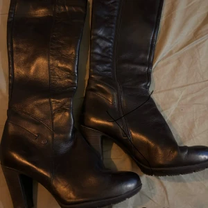 Svarta stövlar med klack från Dasia - Säljer ett par svarta stövlar från Dasia i storlek 39. De är tillverkade i skinn och har en hög klack samt rund tå. Stövlarna har dragkedja på insidan för enkel på- och avtagning. Snyggt och stilrent val för dig som gillar klassiska boots.