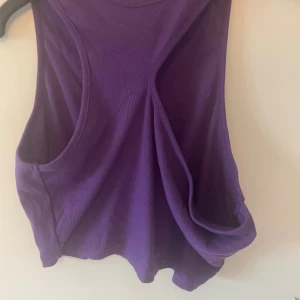 Lila ribbad linnetopp från SHEIN - Säljer en lila ribbad linnetopp från SHEIN i storlek XL. Toppen har en cool asymmetrisk design med breda axelband och stora ärmhål. Materialet är stretchigt och mjukt, perfekt för en trendig och avslappnad look.