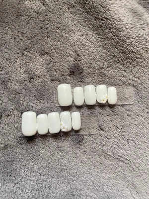 Vita lösnaglar med 3D-blommor - Säljer ett set vita lösnaglar med glansig finish och rundad form. Några naglar är dekorerade med söta 3D-blommor och små gulddetaljer. Perfekt för dig som vill ha en clean och söt look. Kommer i flera storlekar för att passa olika naglar.