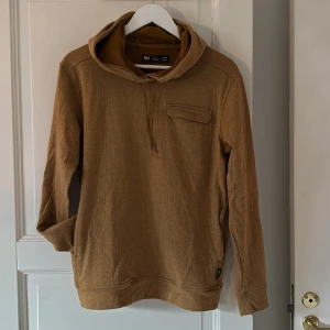 Senapsgul hoodie från Helly Hansen M - Säljer en senapsgul hoodie från Helly Hansen i storlek M. Tröjan har huva med snörning, en bröstficka med lock och är tillverkad i mjuk bomull. Perfekt för chill dagar och har en avslappnad passform med långa ärmar. Fickor på båda sidor. 