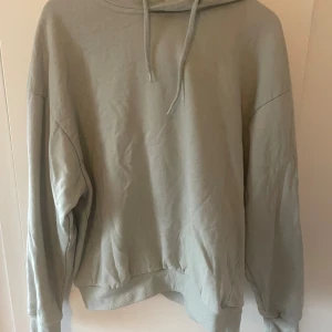 Ljusgrå hoodie från 157, storlek M - En stilren ljusgrå hoodie från 157 i storlek M. Tröjan har huva med snörning och långa ärmar, samt ribbade muddar vid ärmslut och nederkant. Perfekt för chill dagar och enkel att matcha med jeans eller mjukisbyxor.