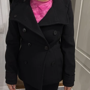 Svart skepparkavaj med knappar - Stilren svart skepparkavaj från H&M i storlek 34 med dubbelknäppning och klassisk krage. Jackan har långa ärmar, figurnära passform och är tillverkad i ullblandning med slät fodrad insida. Perfekt för dig som gillar en tidlös look och vill ha något som funkar hela hösten och vintern. Jackan är aldrig använd. 