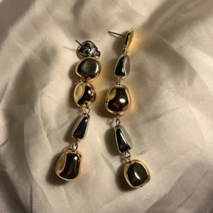 Långa örhängen i guld och silver - Säljer ett par coola långa örhängen med oregelbundna, blanka former i både guld och silver. De har en modern och edgy vibe med metallisk finish och sitter snyggt på örat. Perfekt för dig som gillar statement-smycken och vill sticka ut.