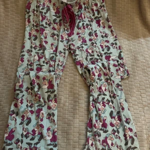 Mjukisbyxor med Disney-mönster - Säljer ett par sköna mjukisbyxor med snörning i midjan och ett färgglatt mönster med Snövit och de sju dvärgarna. Byxorna är ljusblå med lila och grå detaljer, perfekta för chill hemma eller sleepover. Mjuk bomullskänsla och loose passform.