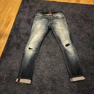 Slim fit Glenn jeans med slitningar - Snygga slim fit Glenn jeans från Jack & Jones i mörkblå tvätt med slitningar och hål som är igensydda från insidan med mörkblått. Perfekt för dig som gillar en modern och edgy look. Storlek 30-32, nypris ca 1000kr. Priset går att diskutera. Använda endast 2-3 gånger av mig och har sedan legat i garderoben.