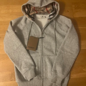 Grå hoodie från Burberry med dragkedja - Snygg grå hoodie från burberry super bekväm o skönt material. Pris går att diskutera! Storlek S men sitter bättre om man har EU XS. Använd 2-3 gånger etikett finns kvar! 