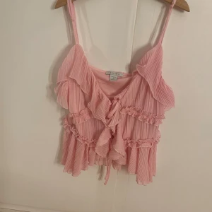 Rosa volangtopp från Amisu - Supersöt rosa linnetopp från Amisu med volanger och smala axelband. Toppen har ribbad struktur. Aldrig använd. Strl M