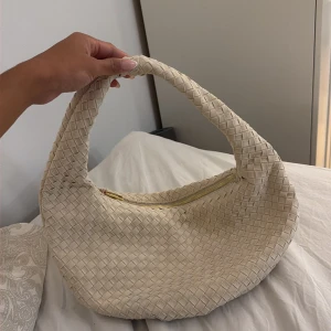 Beige axelväska i flätad mocka - Snygg beige axelväska med flätad design och mjuk form. Väskan har ett stort fack med dragkedja och är tillverkad i mocka. Perfekt för dig som gillar trendiga accessoarer med unik struktur.